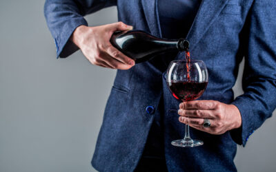 Red wine is poured from bottle to glass. Gourmet drink bottle, red wine glass, sommelier, tasting. Waiter pouring red wine in a glass. Sommelier man, degustation, winery, male winemaker